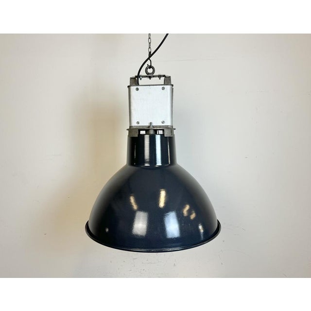 This industrial lamp was made by mazda in france during the 1960s. It features a dark blue enamel shade with white enamel...