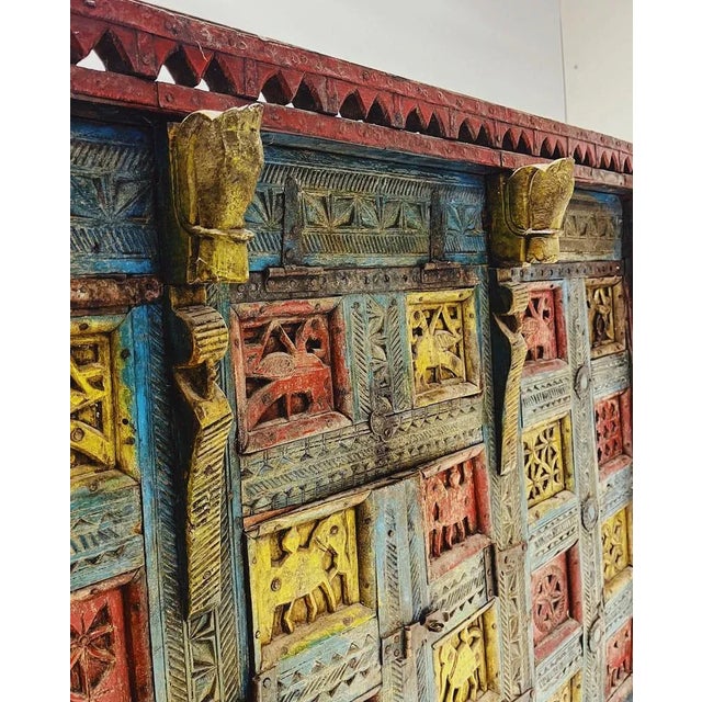 Unique antique teak wood cabinet on functional wooden wheels. The front is richly adorned with intricate wood carvings and...