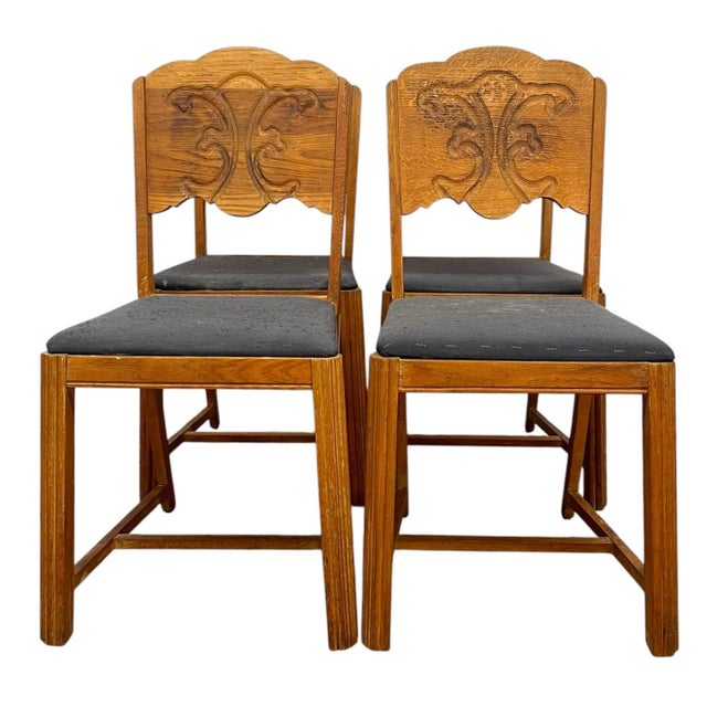 Vintage set of four oak dining chairs featuring carved decorative backrests with stylized scroll and foliate-inspired...