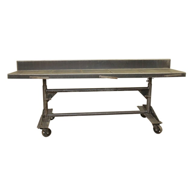 Large steel industrial rolling desk or worktable with height adjustable legs and original four casters. The backsplash...