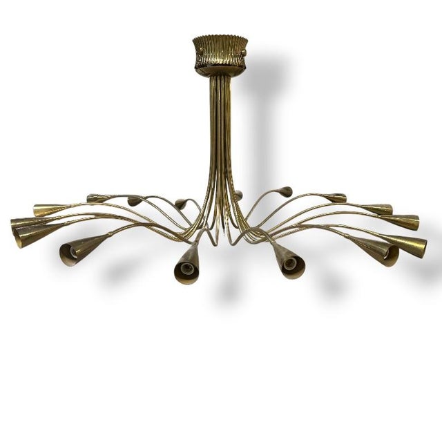 A monumental 16-light mid-century modern brass chandelier featuring sweeping curved arms ending in conical trumpet shades....