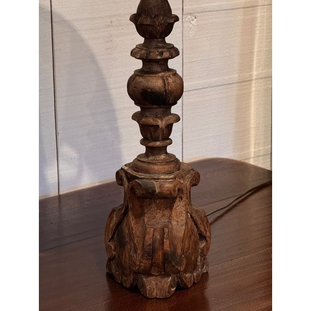 A pair of carved wooden altar stick lamps with tall turned shafts rising from heavy bases carved with leaf forms and...