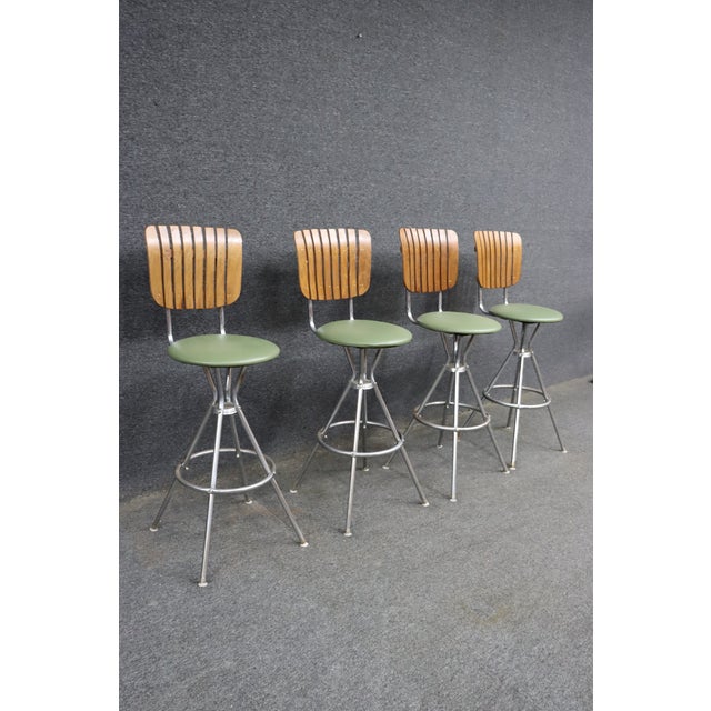 Set of four mid-century modern bar stools featuring sculpted slatted walnut backs, olive green upholstered seats, and...
