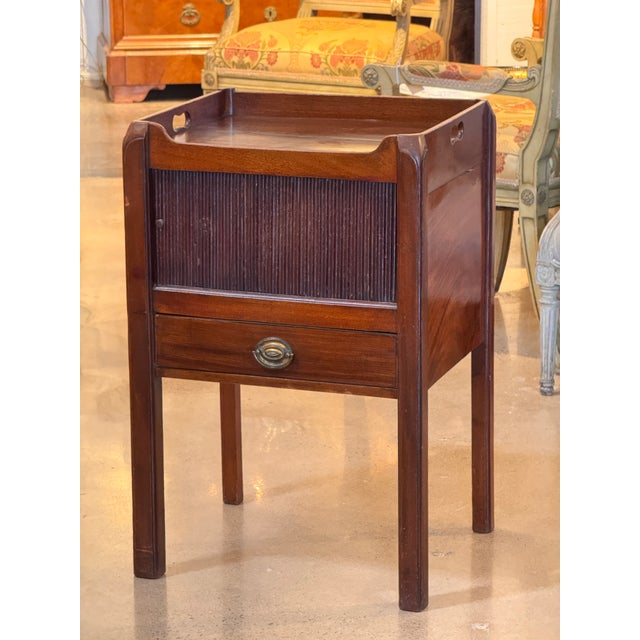 Mahogany bedside commode with a raised gallery top, shaped corner posts, and a tambour front panel above a single drawer...