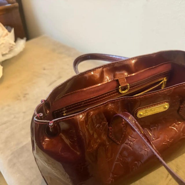 This sophisticated Louis Vuitton Wilshire hand bag is meticulously crafted from the house's iconic Monogram Vernis patent...