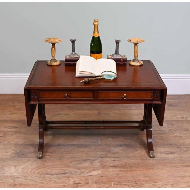 Elegant Regency style coffee table crafted from mahogany Inset tooled leather top with gilt detailing Drop leaves extend...