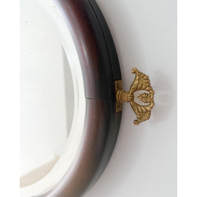 Antique Regency style oval wall mirror with a rich mahogany frame, beveled-edge glass, and decorative brass finial details...