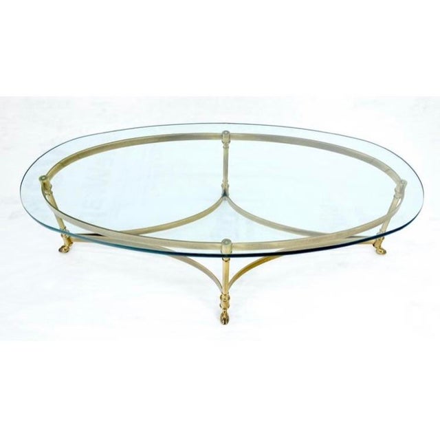 This MCM/ Hollywood Regency style brass and glass coffee table has a light and airy silhouette. Featuring stylized hoof...