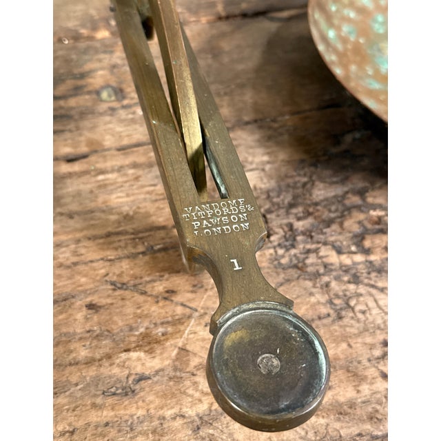 This antique English brass apothecary balance scale by Vandome Titford & Pawson of London features a classic dual pan...