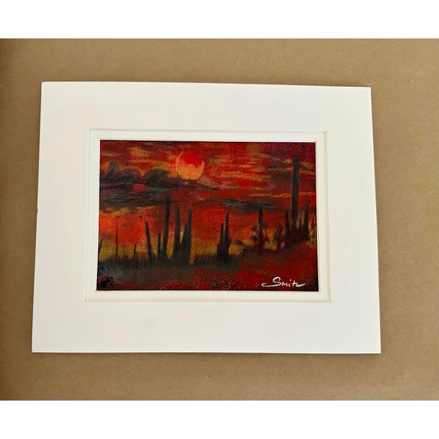 An evocative original landscape capturing the dramatic beauty of the desert at sunset. A glowing orange-red sun hangs...