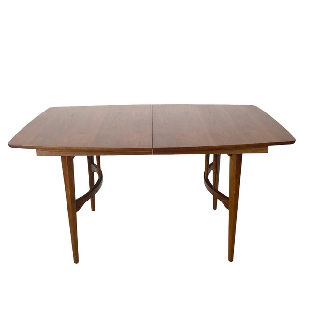 This walnut dining table pairs a clean, rounded-corner top with a distinctly sculptural base — tapered legs joined by a...