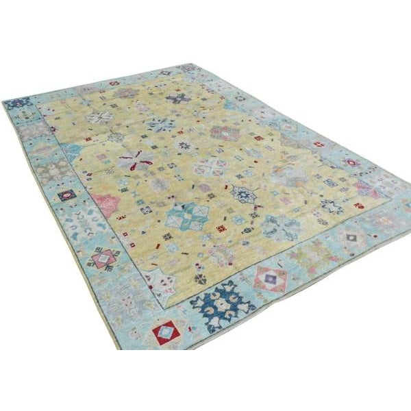 A distinctive modern Oushak rug featuring a soft light yellow field framed by a pale blue border, with stylized floral...