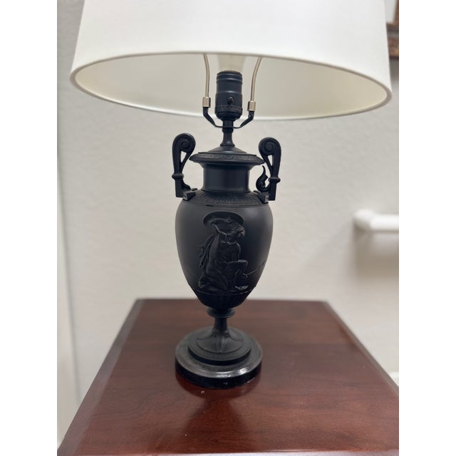 A refined and sculptural pair of neoclassical-style table lamps featuring black cast metal urns with classical relief...