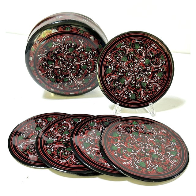 This 1960s Japanese lacquerware coaster set features intricate floral decoration, rich red and green tones, and a fitted...