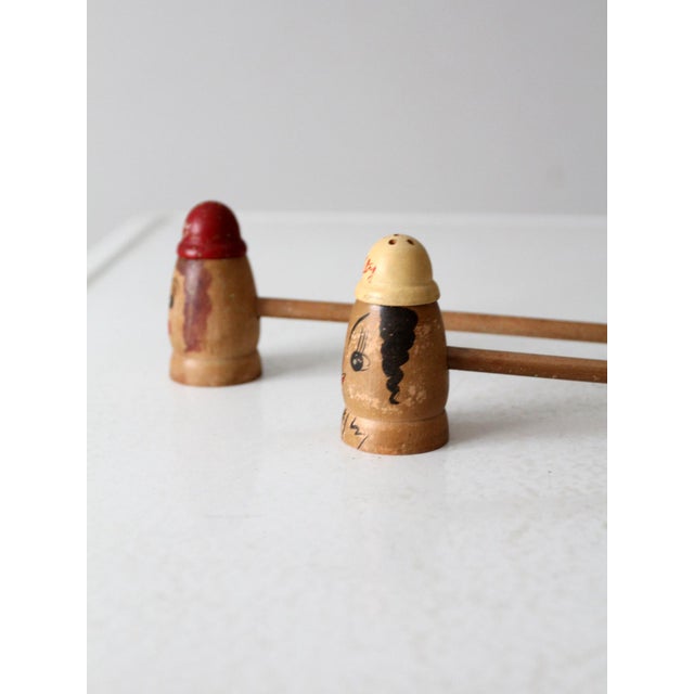 A mid century pair of wooden salt and pepper shakers with hand painted faces and extra long turned wood handles, labeled...