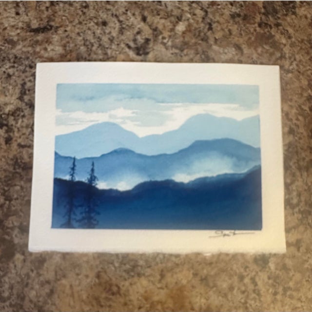 Cool blue layers of distant mountains fade into the sky, creating a peaceful sense of depth and atmosphere. A beautiful...