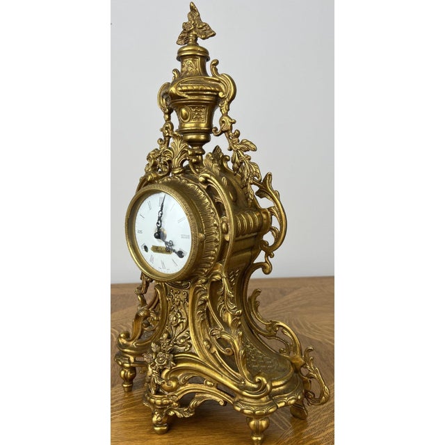 A stunning Vintage brass clock featuring an exceptionally ornate Rococo-inspired design with elaborate scrollwork,...