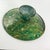 A shallow green stone bowl raised on a turned pedestal foot, with richly varied tones of deep green, teal, and cream...
