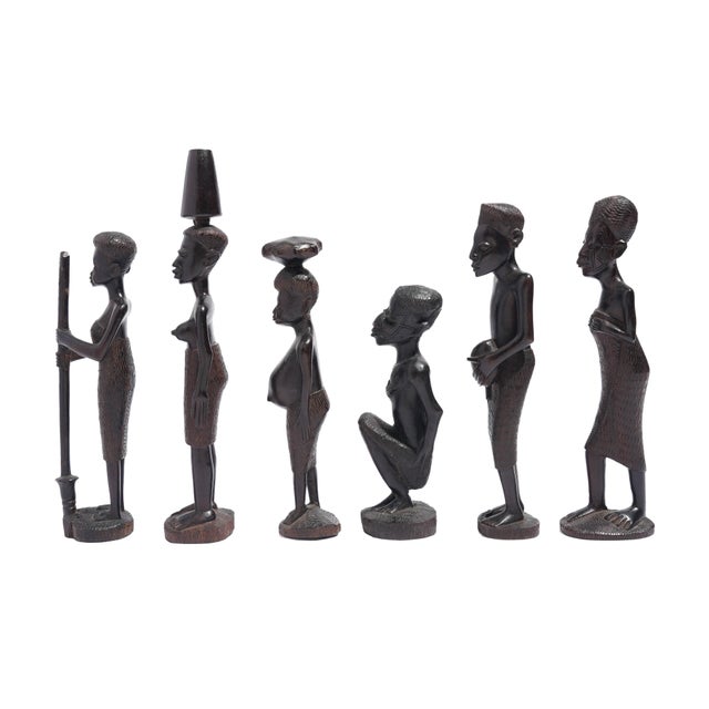 A set of six carved ebony figures from Kenya, 1950-70, each depicting a different moment of village life. One figure grips...