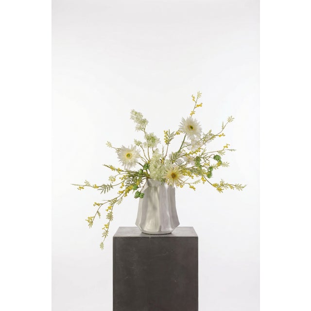 An airy, light-filled arrangement of white and pale yellow gerbera, mimosa, and delicate greenery. The extended stems...
