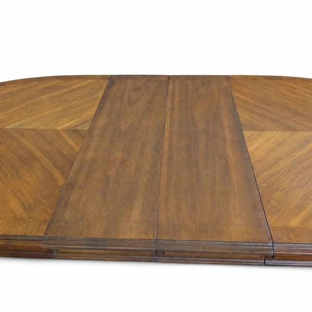 A 1960s Drexel Esperanto oval extension dining table with a warm walnut-veneer top, a four-part chevron grain composition...