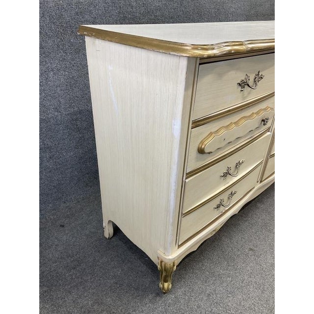An elegant vintage French Provincial triple dresser featuring its classic cream finish, gilded gold detailing and...