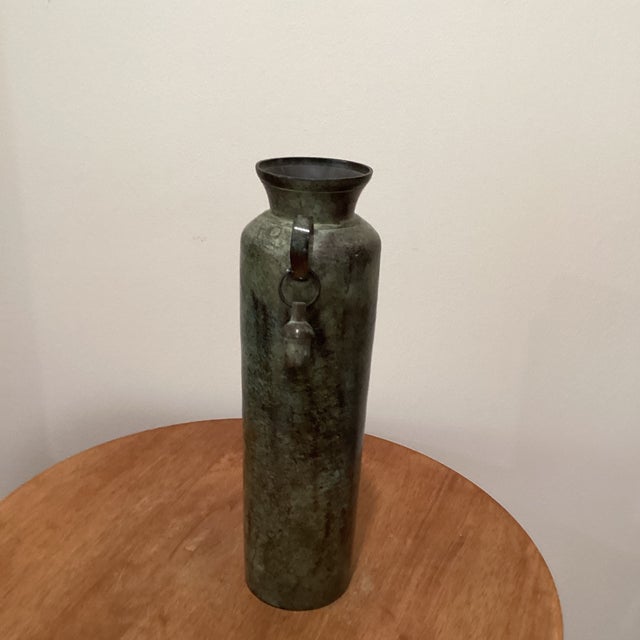 This vintage cylindrical metal vase/vessel features unique dangling bell handles, adding a touch of charm and whimsy to...