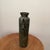 This vintage cylindrical metal vase/vessel features unique dangling bell handles, adding a touch of charm and whimsy to...