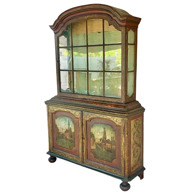 A Dutch Polychrome Painted Cabinet. The upper section has a shaped bonnet top with a gently arched crest that adds...