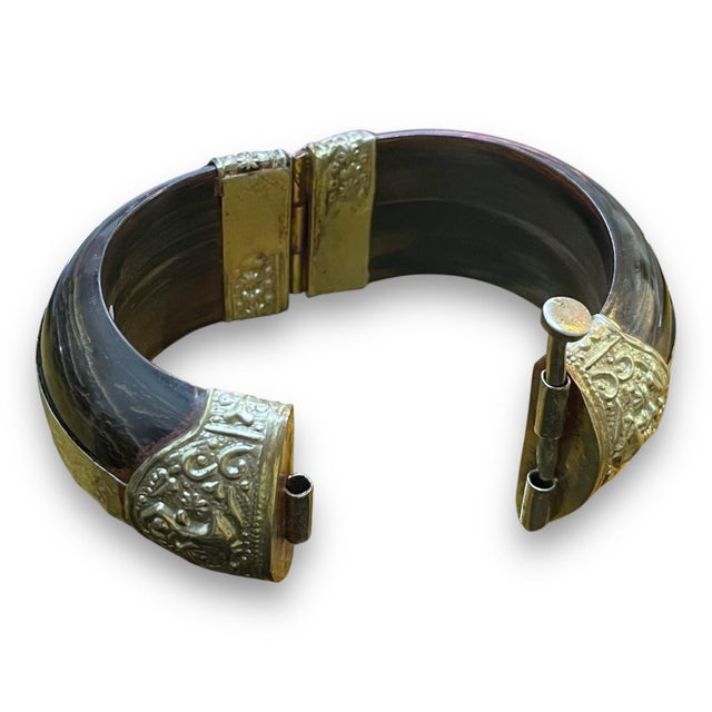 This bracelet showcases a striking design with intricate engravings on a dark, polished base. The detailed floral patterns...