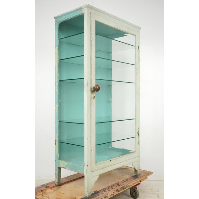 Early to mid-20th century steel display case with glass sides and shelves. The exterior is partially painted white, along...