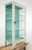 Early to mid-20th century steel display case with glass sides and shelves. The exterior is partially painted white, along...