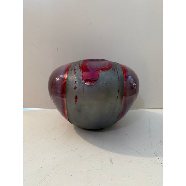 A striking vintage art pottery vessel featuring a low, rounded form with a dramatic metallic raku-style glaze. Deep red...
