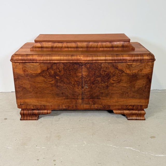 A refined cabinet featuring elegant, rounded detailing in the Art Deco style. It is finished in walnut, treated with...