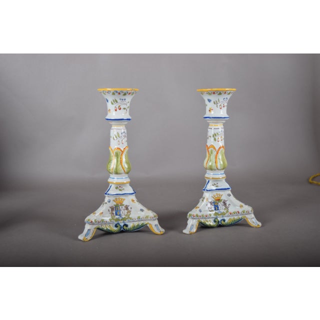 Pair of hand-painted ceramic candlesticks from the 1910s. Each has a flared footed base, scalloped edges, blue, yellow and...