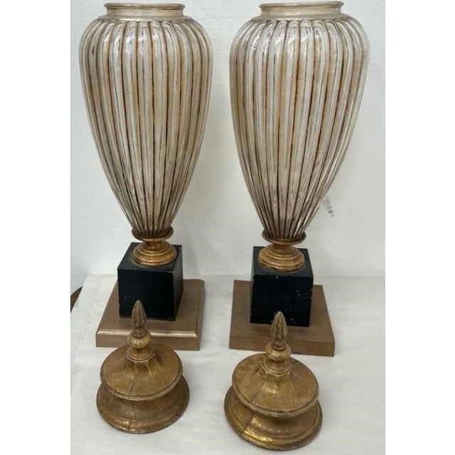 An elegant pair of Neoclassical-style covered urns featuring elongated ribbed glass bodies with a softly antiqued cream...