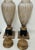 An elegant pair of Neoclassical-style covered urns featuring elongated ribbed glass bodies with a softly antiqued cream...