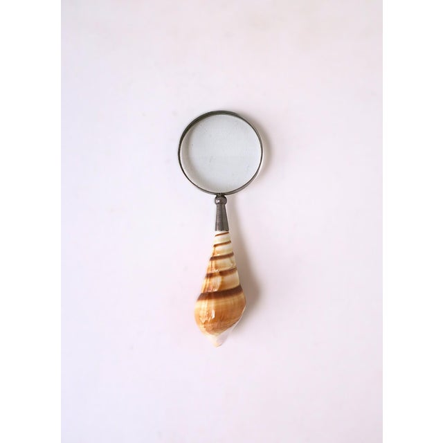 A metal magnifying glass with seashell handle, circa early to mid-20th century. Piece has a metal frame with what appears...
