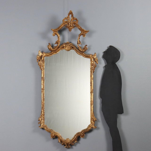 Carved and gilded wooden mirror. The molded frame is embellished with Rocaille leaf carvings, and the canopy is carved...