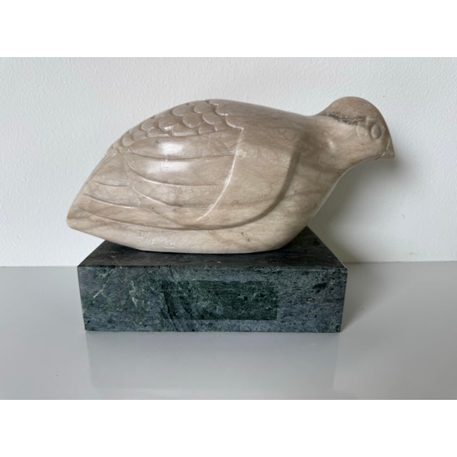 A beautifully hand-carved marble bird sculpture depicting a stylized dove, resting gracefully atop a solid green marble...