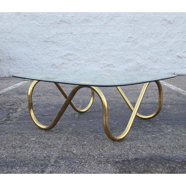 Striking vintage coffee table featuring a fluid, articulating, tubular brass base with a sculptural, looping form. The...