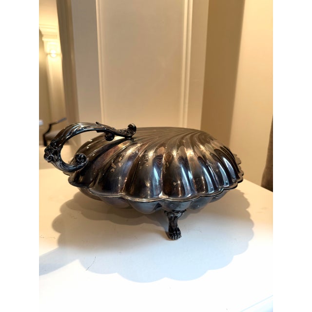Vintage silver-plated scallop shell warming dish, often used for serving seafood or as a decorative centerpiece, features...