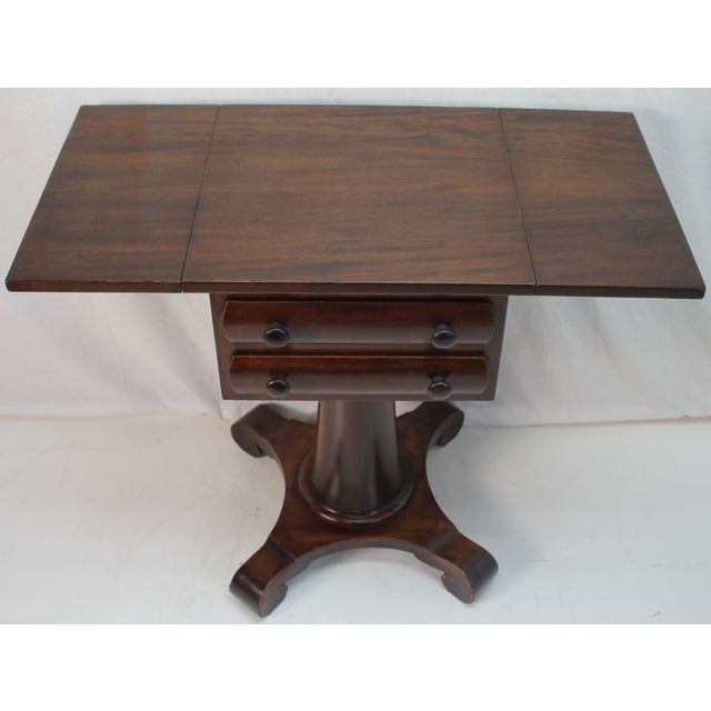 This elegant 1920s American Empire drop-leaf side table exudes timeless sophistication with its rich mahogany finish. The...