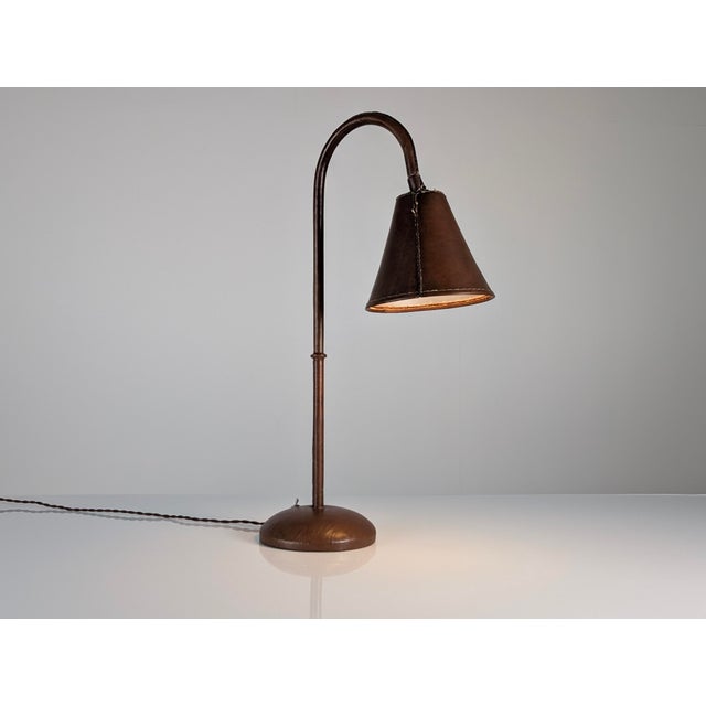This table lamp was designed by French modernist Jacques Adnet in the 1950s. The tubular stem, round base, and conical...