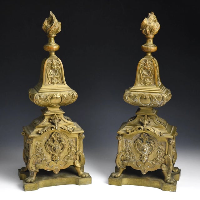This pair of authentic antique bronze andirons showcase a Régence theme of flaming baluster vases at their top, along with...