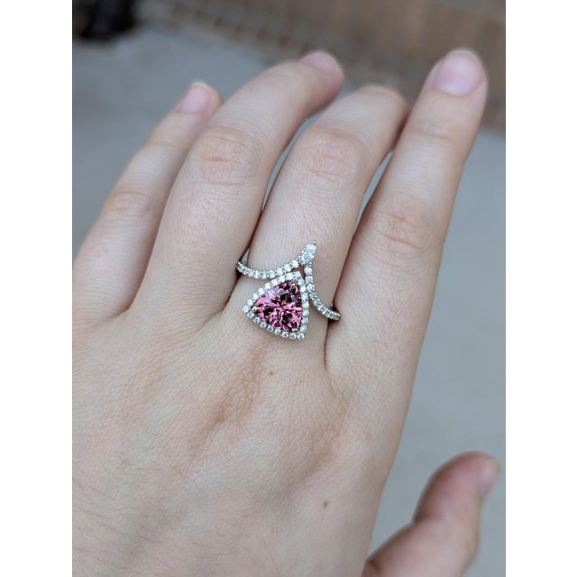 This striking ring features a 1.70ct trillion-cut pink tourmaline, measuring 8mm, set in a shimmering diamond halo that...