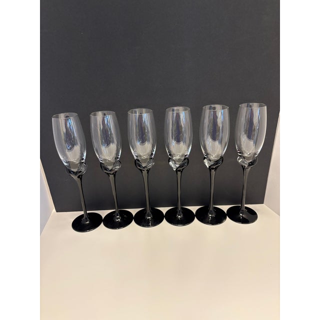 A striking set of six modern champagne flutes featuring glossy black stems with sculptural twisted knot detailing and tall...
