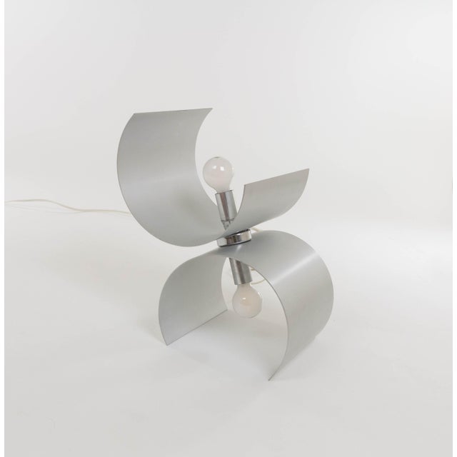 Table lamp produced by Nucleo Sormani in the 1970s. The lamp consists of two curved aluminum parts, both containing a...