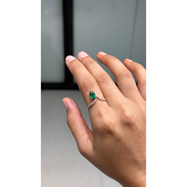 This handcrafted bypass solitaire ring showcases a 0.7 carat natural oval zambian emerald, set in 14K yellow gold. The...