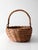 A vintage woven gathering basket with a bent bamboo handle, oval form, and tightly woven wicker body in rich honey brown...